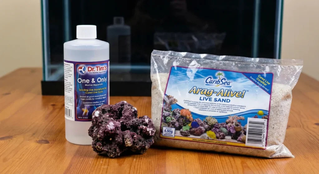 How To Cycle a New Marine Aquarium Safely, Quickly, and On a Budget 5 A photograph showing the three main sources of beneficial bacteria for seeding a marine aquarium sitting on a wooden table: a bottle of Dr. Tim's One & Only nitrifying bacteria, a piece of mature purple live rock, and a bag of CaribSea Arag-Alive live sand.